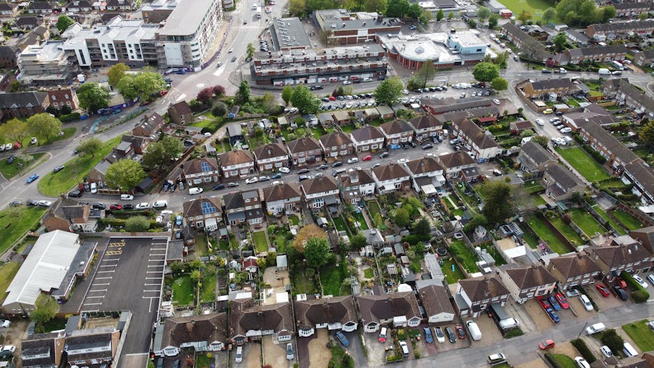 An aerial view of a residential neighbourhood showing rows of semi-detached houses with small, well-maintained gardens and backyards, some featuring solar panels on the roofs. The houses are separated